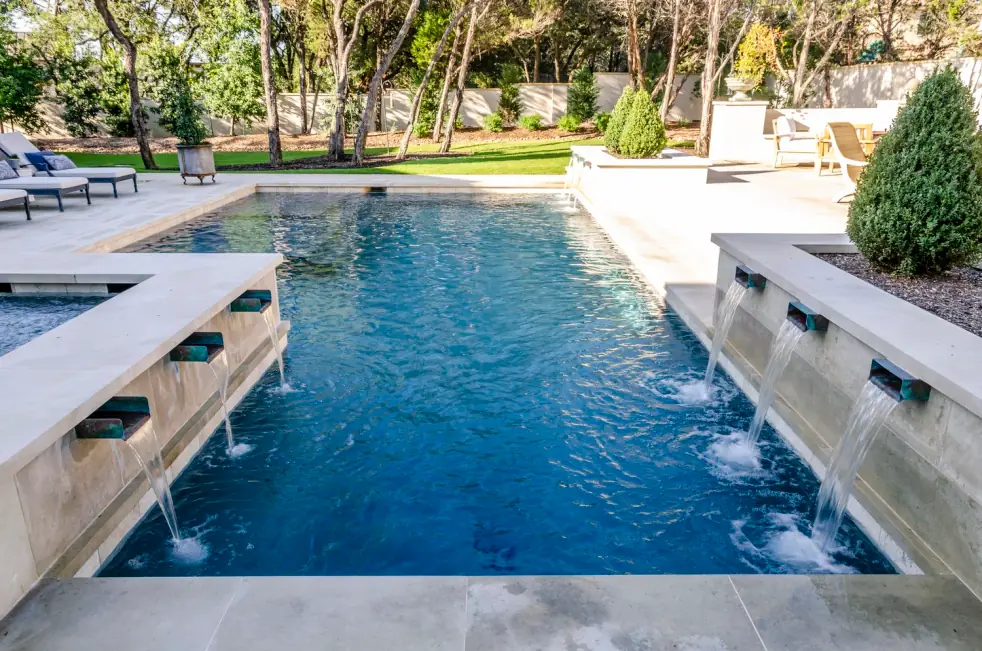 Dark-finish pool with copper scupper waterfalls falling from limestone walls under live oaks