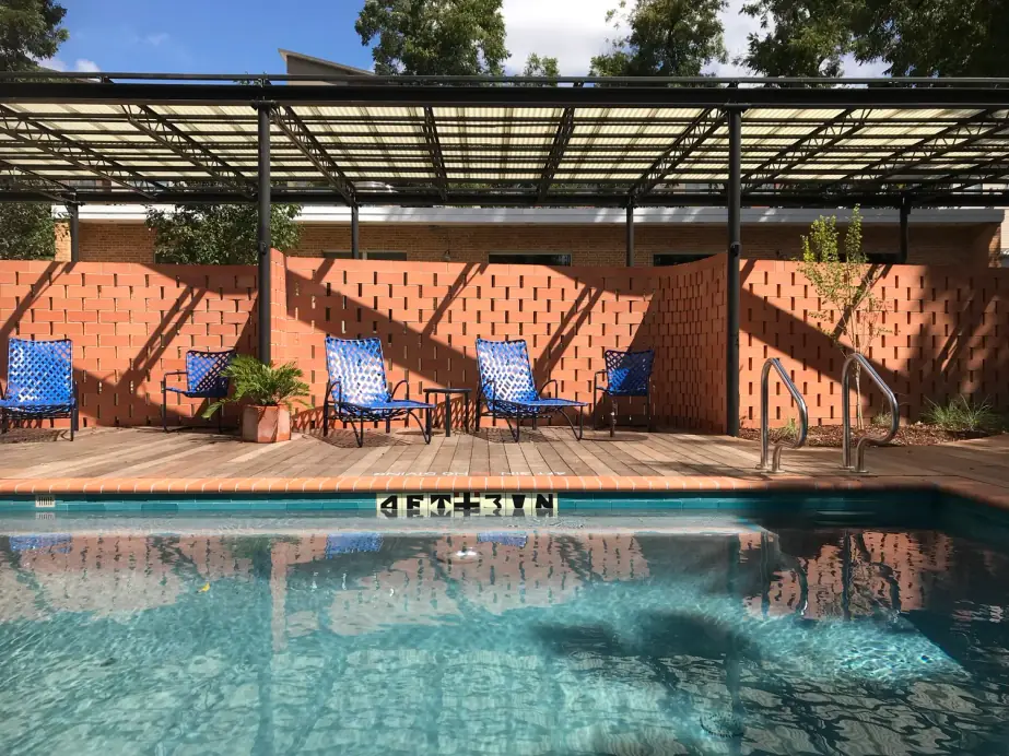 Boutique hotel pool with a terracotta brick screen wall, blue loungers and a steel pergola
