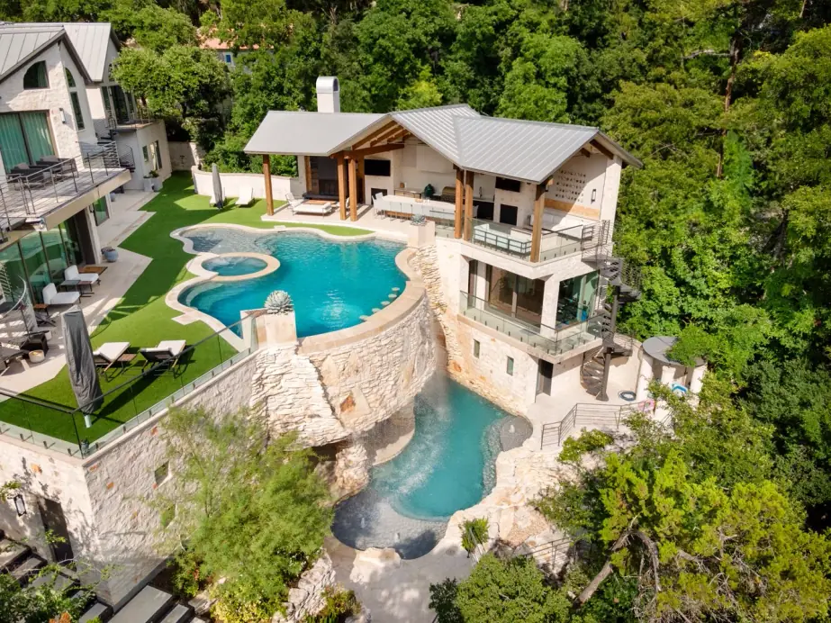 Aerial of a cliffside residence with an upper pool above a stone-faced drop to a grotto pool
