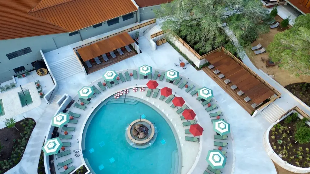 Aerial view of a circular spa pool with a centre rock fountain, loungers and red umbrellas