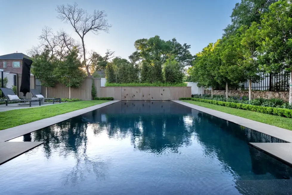 Black-bottom lap pool with still water reflecting the trees and sky