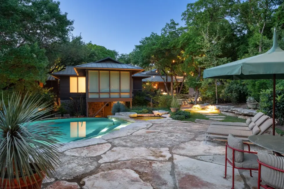 Pool beside a treehouse-style home at dusk with flagstone terrace and uplit trees